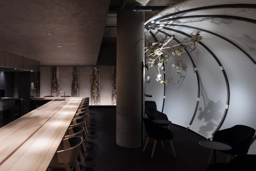 Interior of a moody, low-lit restaurant with a long empty table and a large column in the room. 