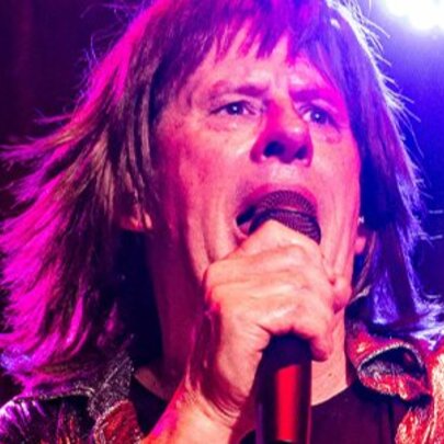 Mick Jagger tribute artist, singing into a microphone backlit by purple and pink lights.