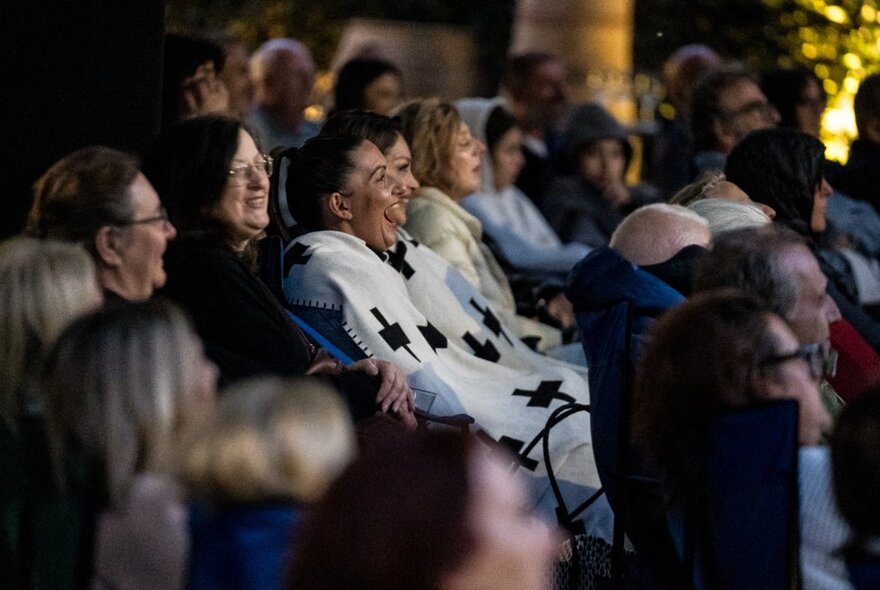 People seated in rows under blankets watching an outdoor screen in the dark.