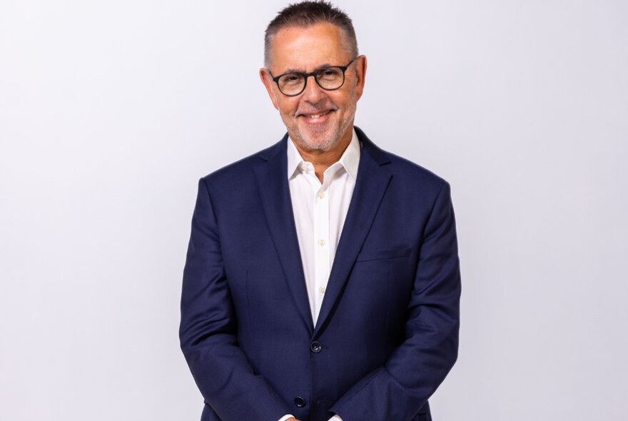 Dr Norman Swan, smiling warmly as he poses against a white wall wearing a blue jacket. 