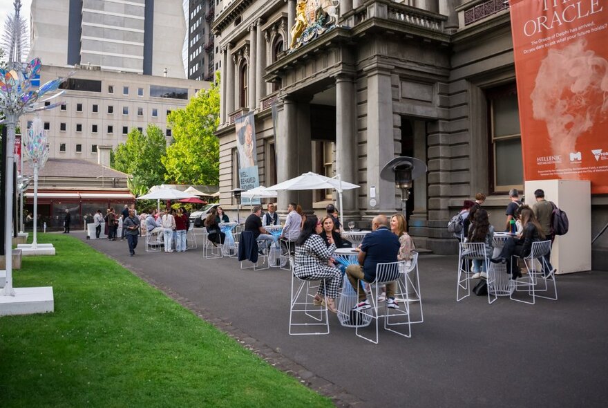 People seated outside in small groups at the Hellenic Museum. 