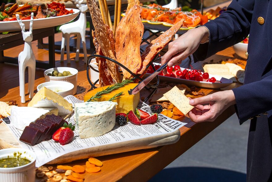 Hands slicing cheese from a selection of cheeses on a festive food display.