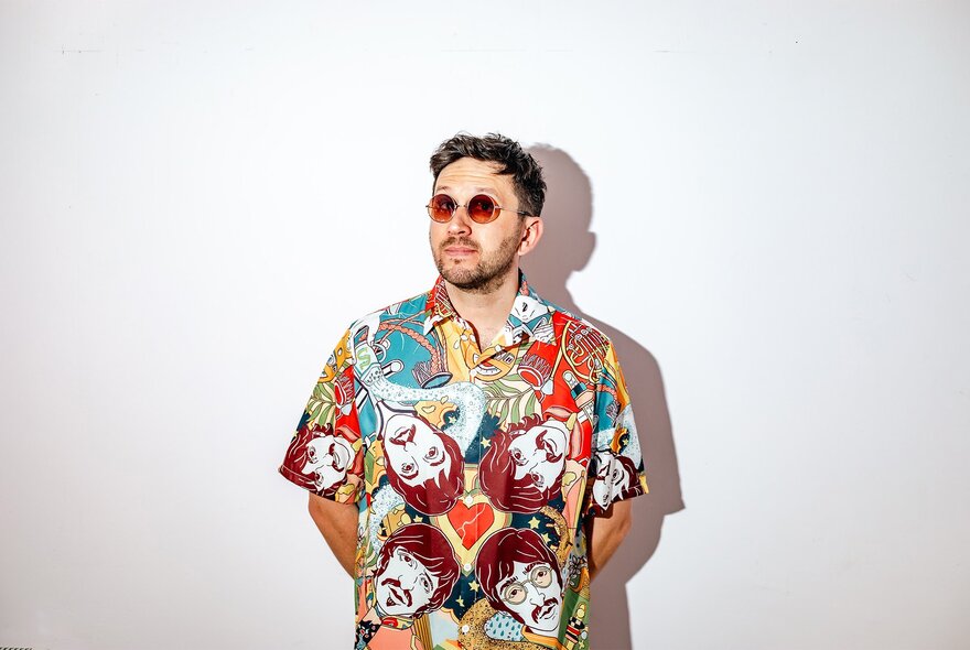 Portrait of UK DJ Chris Arnold, wearing a loud shirt with The Beatles' faces on it and sunglasses; his hands behind his back. 