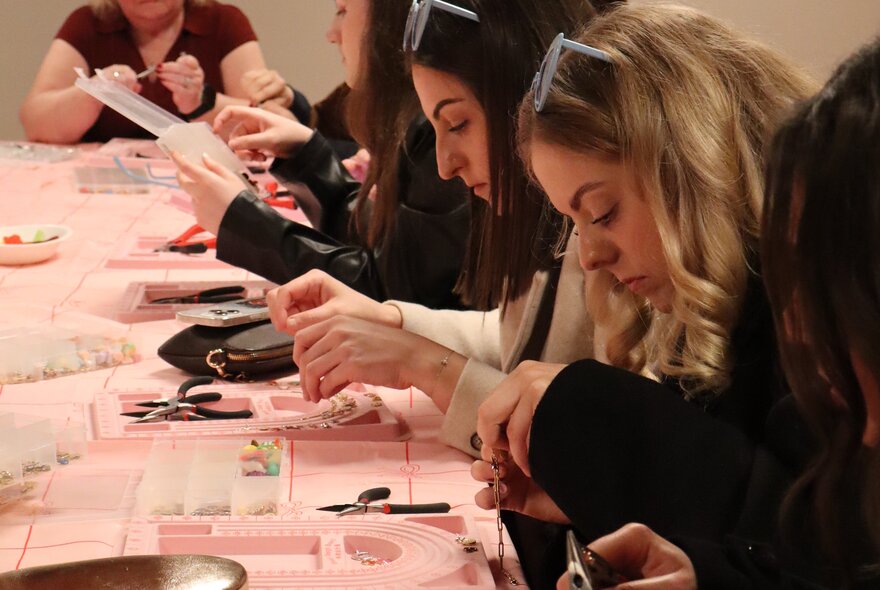 A workshop with women at a table with a pink tablecloth working on projects. 