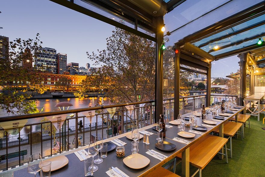 The outdoor balcony terrace at Hophaus with tables set for dinner service, and views over the Yarra river and city skyline at dusk.