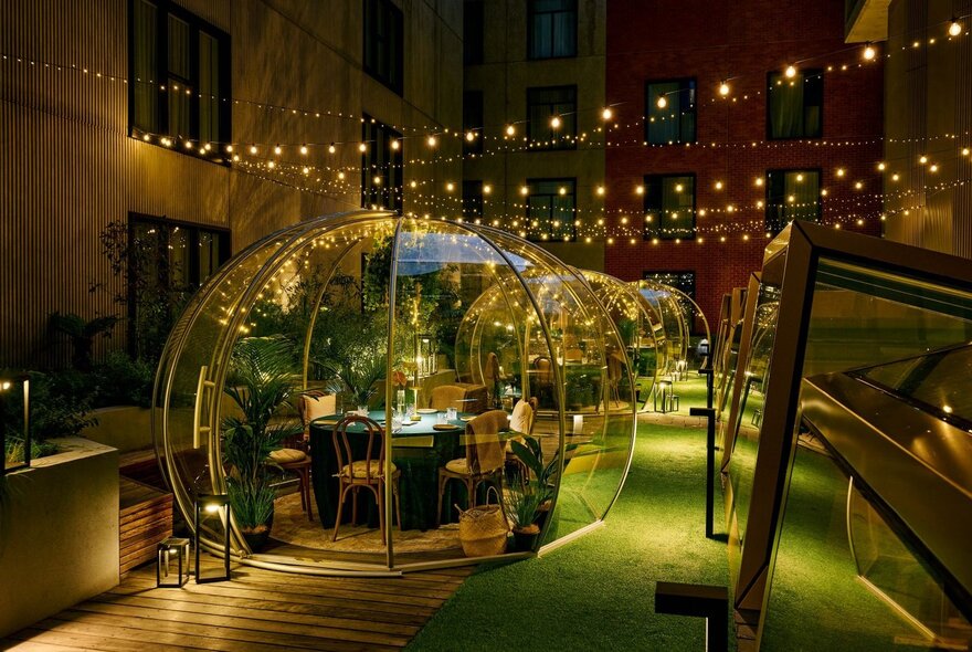 Private dining bubbles in a designed space with greenery and fairy lights.