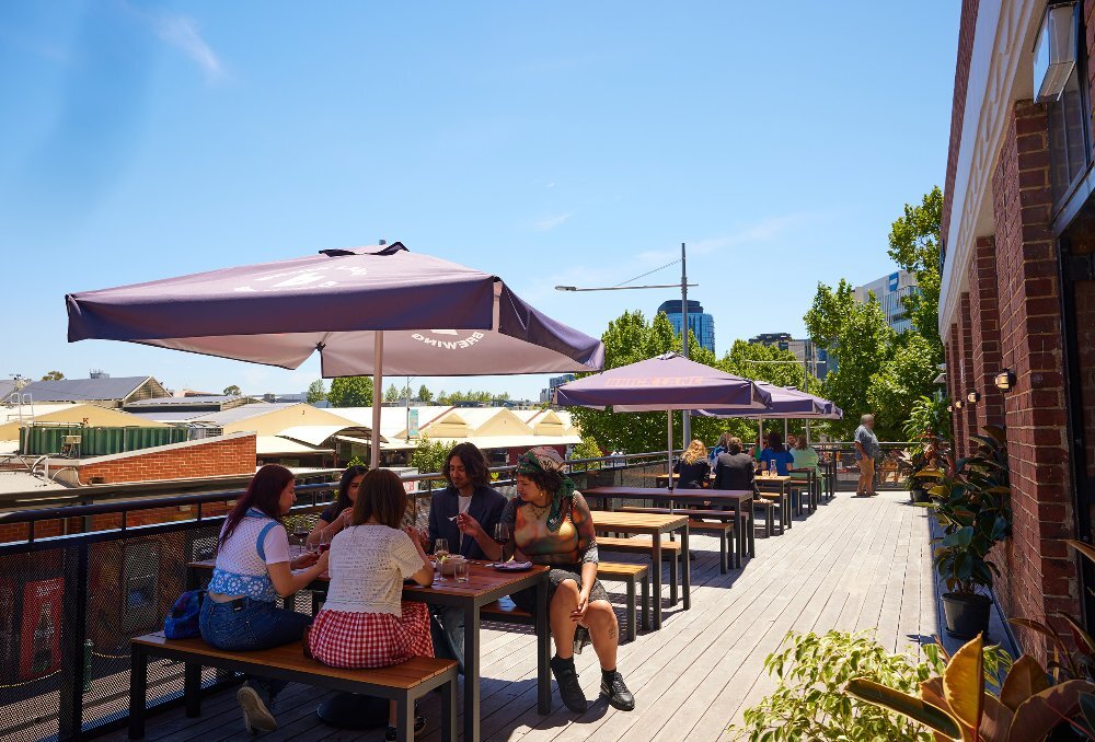 A group of friends are at a rooftop pub in the sun. 