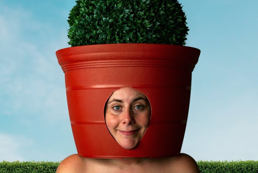 A woman wearing a pot plant on her head, her face showing through a cut-out section in the base. 