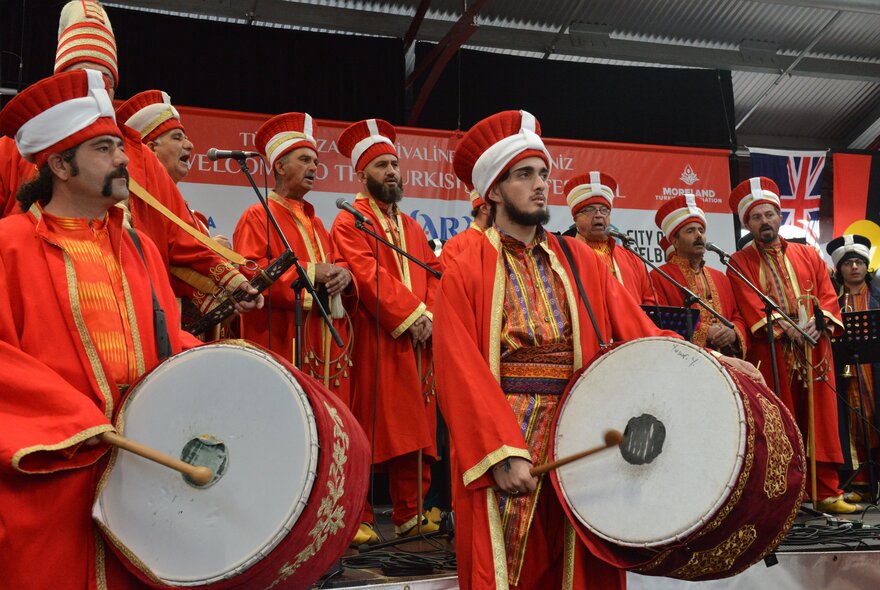 A group of tradtional Turkish muscians in red costumes, two with large drums. 