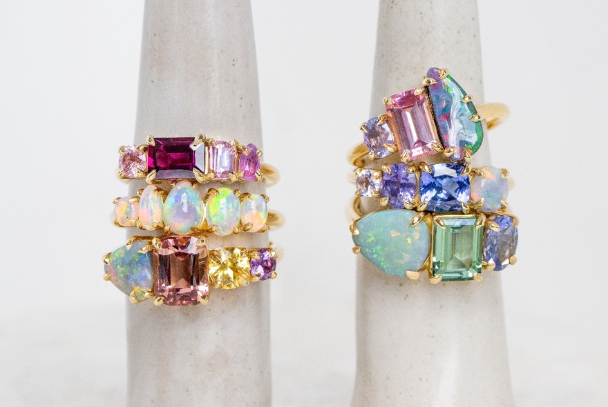 Six rings set with colourful gems and opals on a ring finger display stand.