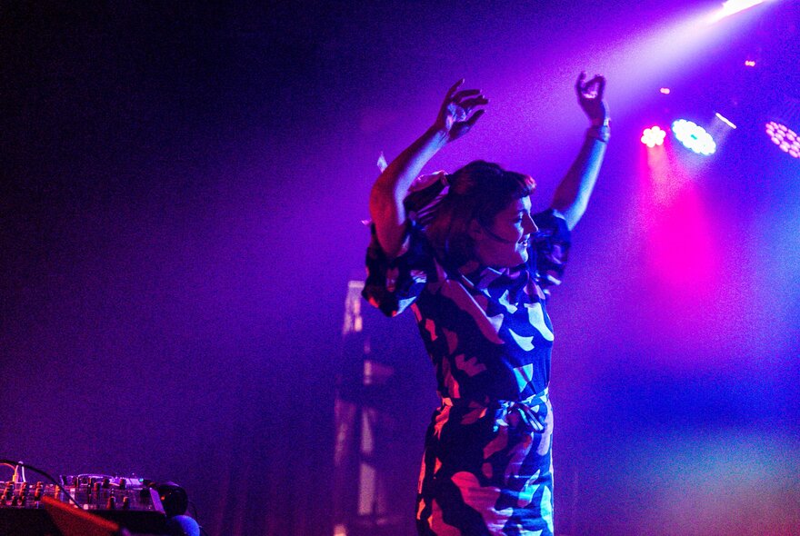 A woman in a nightclub dancing with arms in the air and pink and blue lights. 