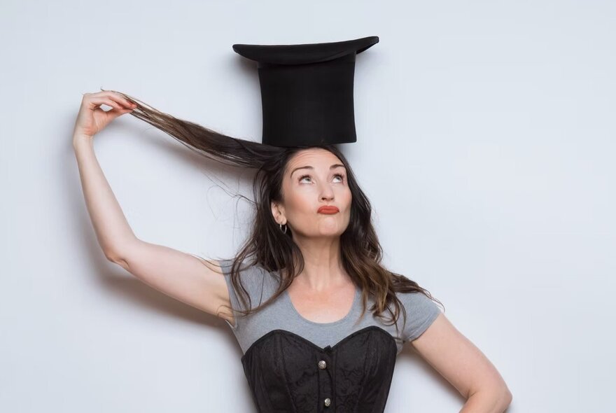 Performer Calista Sinclair wearing a black top hat and pulling up her long hair with one hand and looking upwards.