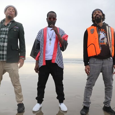 The three members of LA hip-hop legends The Pharcyde, standing in strong poses on a beach.