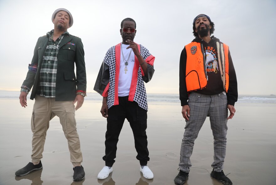 The three members of LA hip-hop legends The Pharcyde, standing in strong poses on a beach.