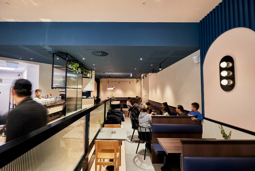 A family dining in a long cafe with blue and pink walls and an open kitchen.