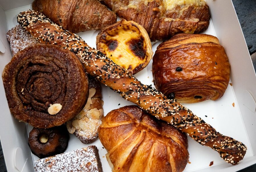 A box of baked products including croissants and tarts.