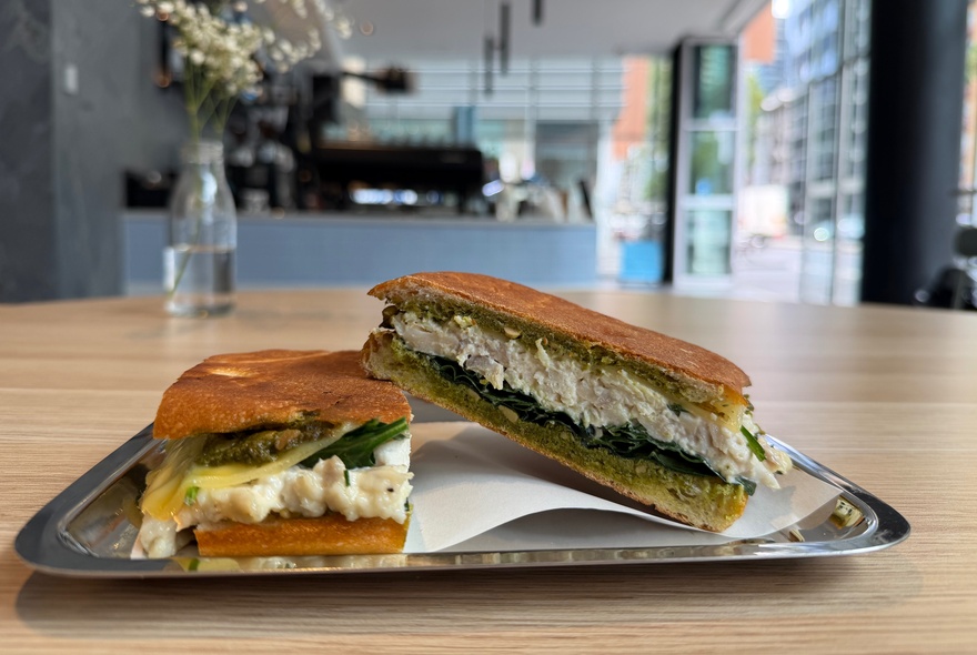 Two halves of a grilled spinach and feta panini served on a silver tray on a table inside a cafe interior.
