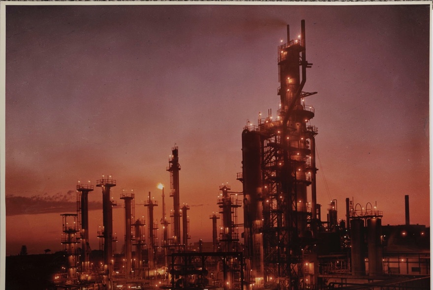 Oil refinery lit up at night against a purple sunset sky.