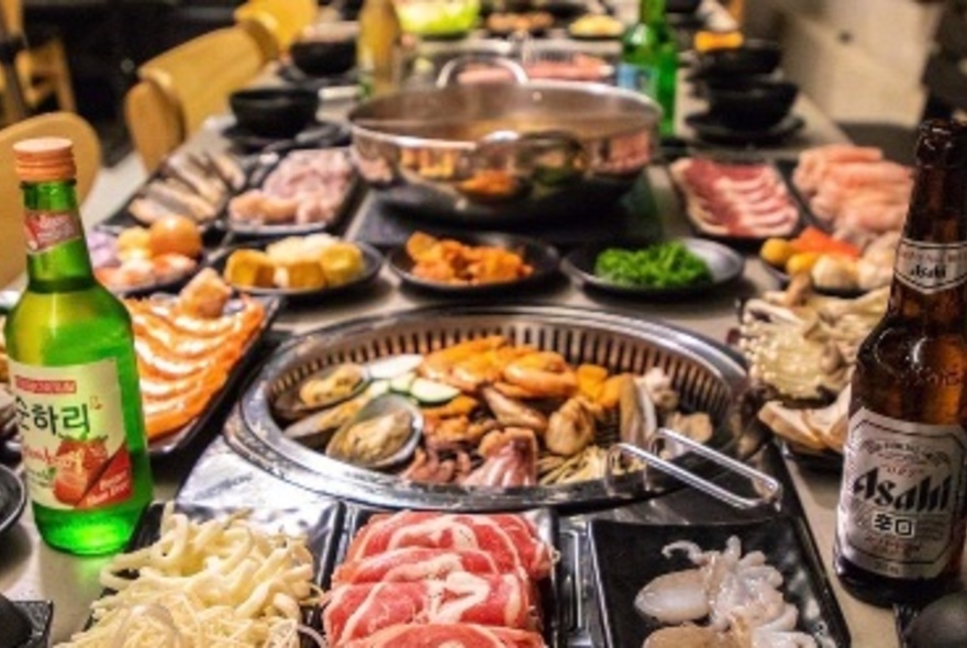 Dining table filled with trays of fresh meats and vegetables, waiting to be cooked in the hot pots at the centre of each table.