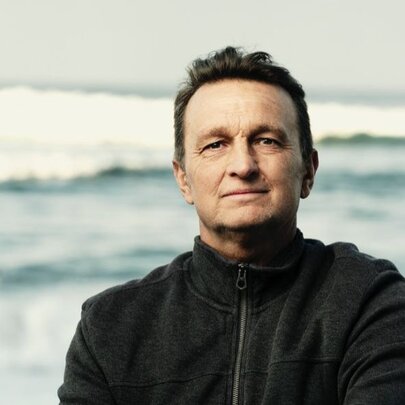 Person standing with waves crashing behind them, wearing a dark windcheater.
