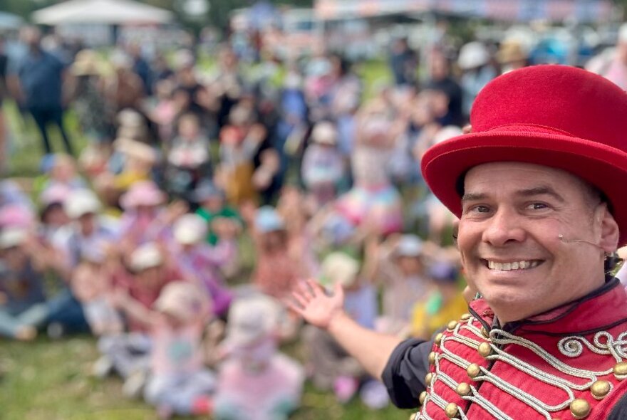 Christ Morant performing outdoors in front of a blurred crowd wearing a red ringmaster's coat and hat. 