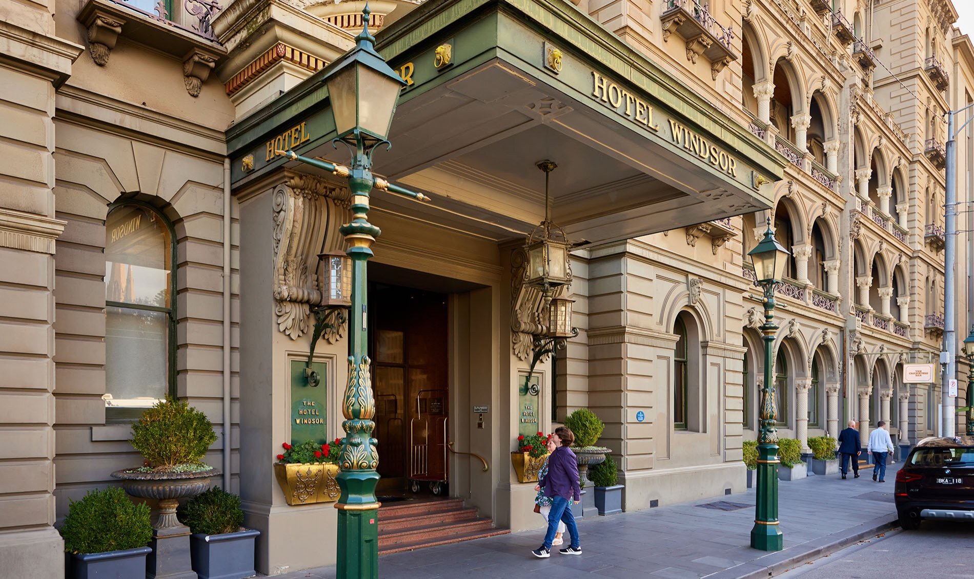 Two people walking into a grand city hotel. 
