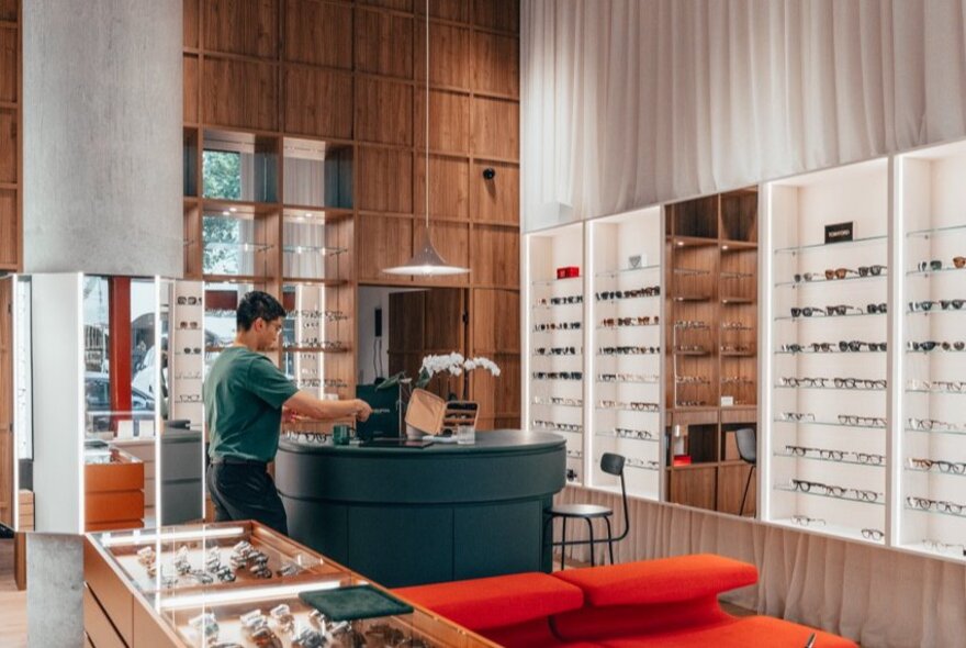 Interior of Seasons Optical, with eyewear on display in cabinets and on the wall, and a person standing at the store counter.