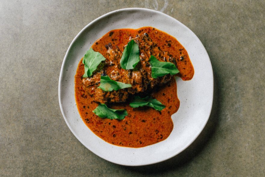 A Indian-style dish with grilled meat served in a curry sauce, presented on a white plate. 