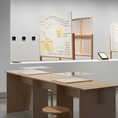 An exhibition installation featuring desks with display cases and informational boards in the background.