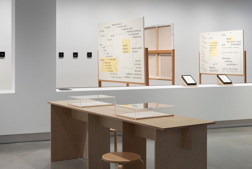 An exhibition installation featuring desks with display cases and informational boards in the background.
