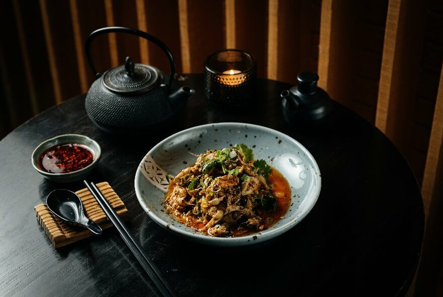 A table set with large bowl Chinese food and a black teapot.