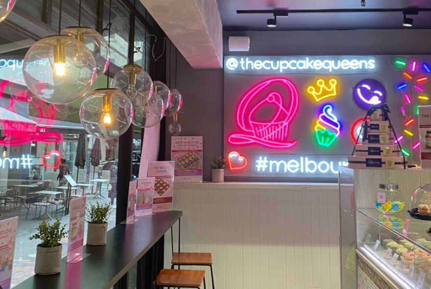 Brightly lit cafe interior with neon lighting, bench seating and a cake display case.