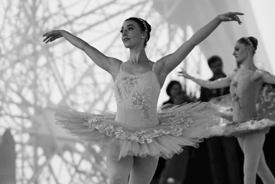 A black and white image of a ballerina in a tutu with arms outstretched. 