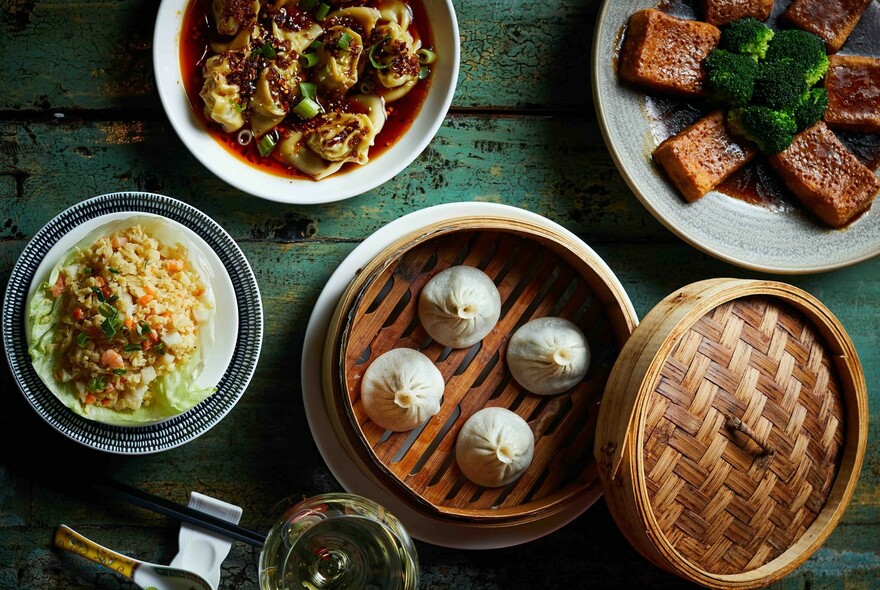 Dumplings in bamboo steamer with dishes including tofu and rice.