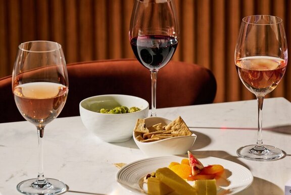 Three glasses of wine on a table with small snack plates of food alongside.