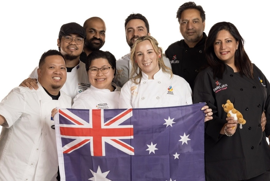 A group of people wearing either white or black chef's outfits, posing with an Australian flag.