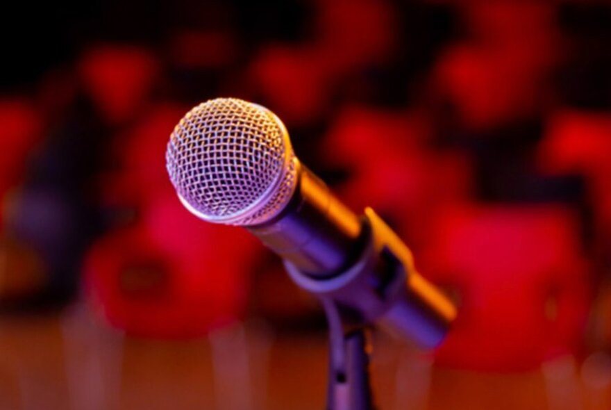Close-up of a microphone on a stand, against a red blurred background.