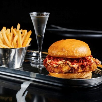 A burger, fries and mini martini served on a silver platter.