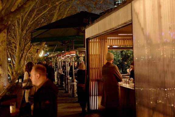 An outdoor restaurant with an outdoor bar and umbrellas alongside trees.