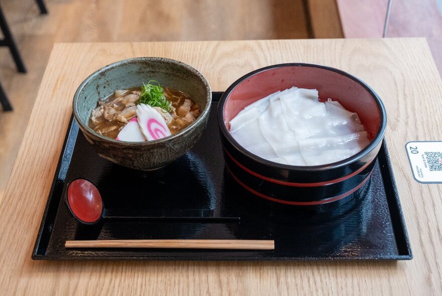 Two bowls of udon noodles on a tray with chopsticks.