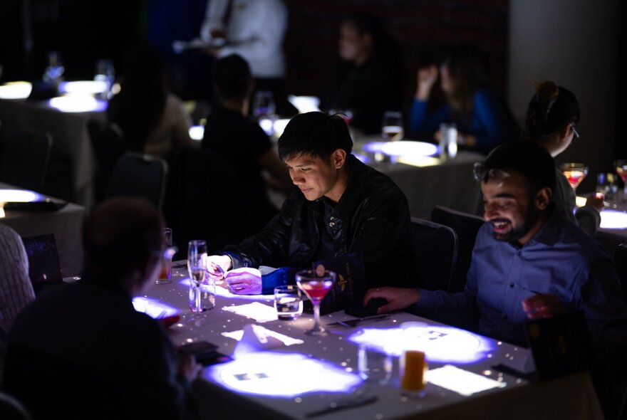 Diners in a darkened restaurant, spotlights playing on their food and drinks.