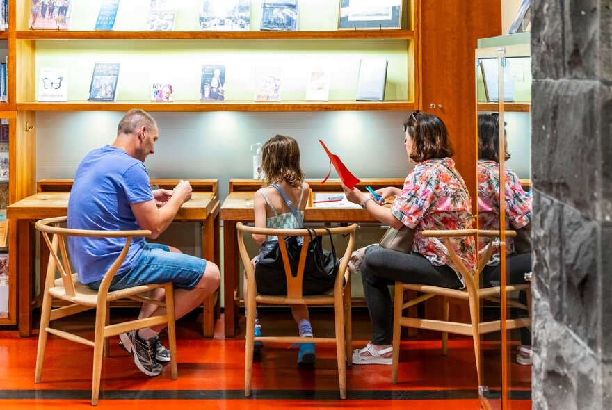 Two adults and a child completing a craft activity at a table inside the Immigration Museum.