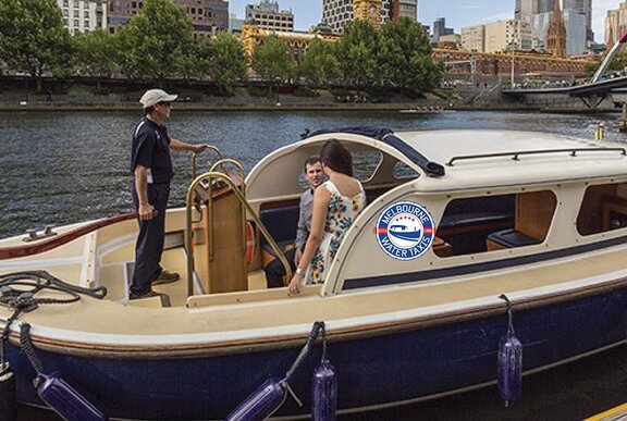 A young couple on a blue and cream boat, with a skipper in black standing on the back.
