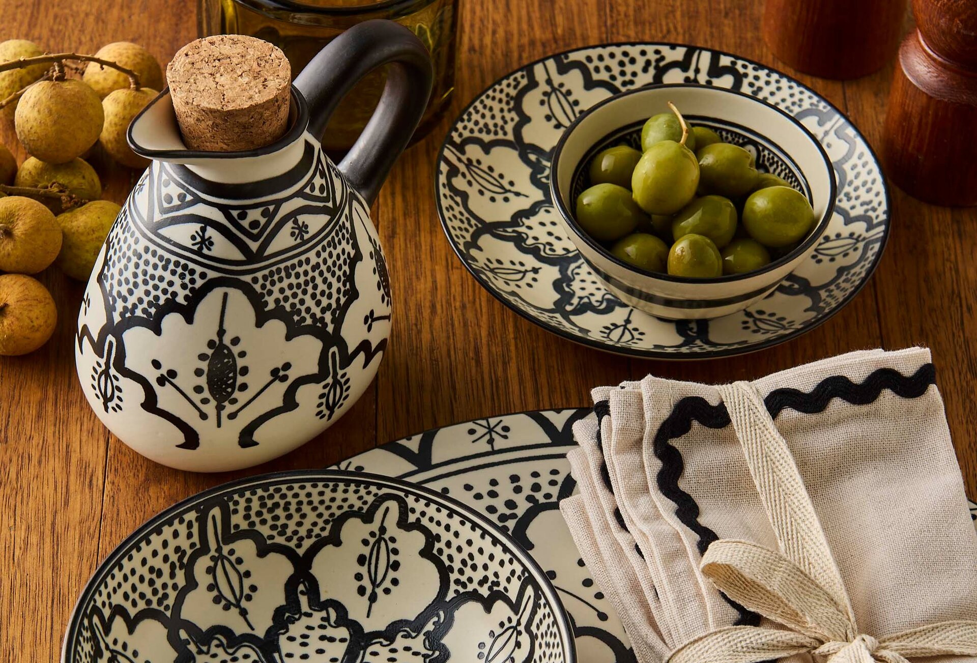 A set of black and white painted ceramic oil jug, plates and bowls with olives.