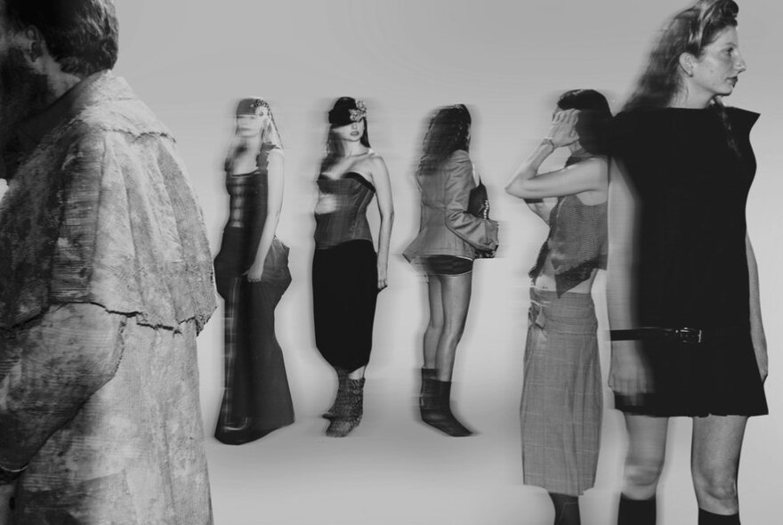 Blurred image of models wearing various outfits standing against white backdrop.
