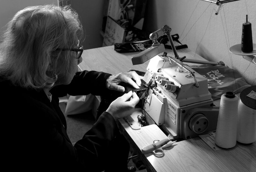 Woman seated at an industrial sewing machine working by dim light. 