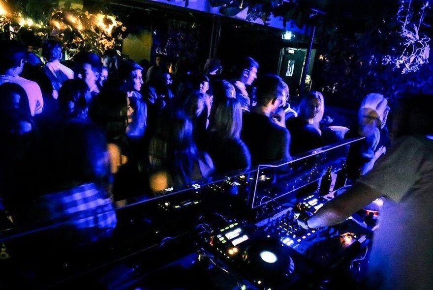 People dancing in a dark nightclub, part of the DJ's mixing desk visible to the right.