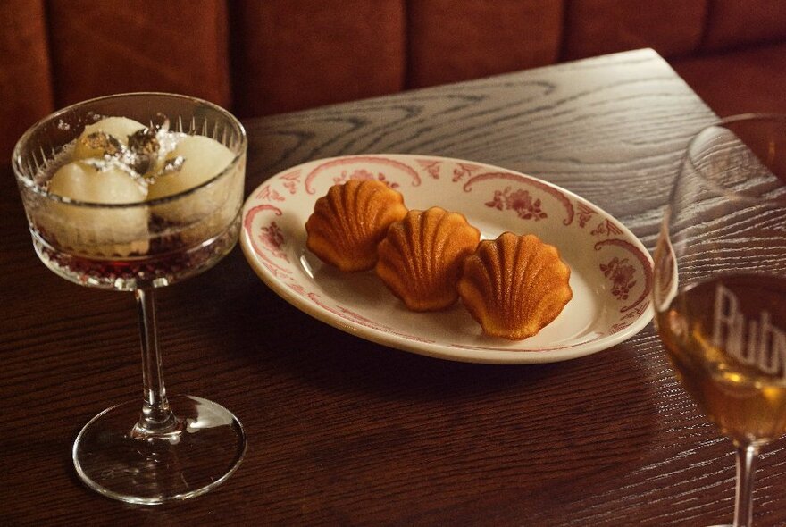 Three madeleines on a plate with a dessert dish of fondants and dessert wine.