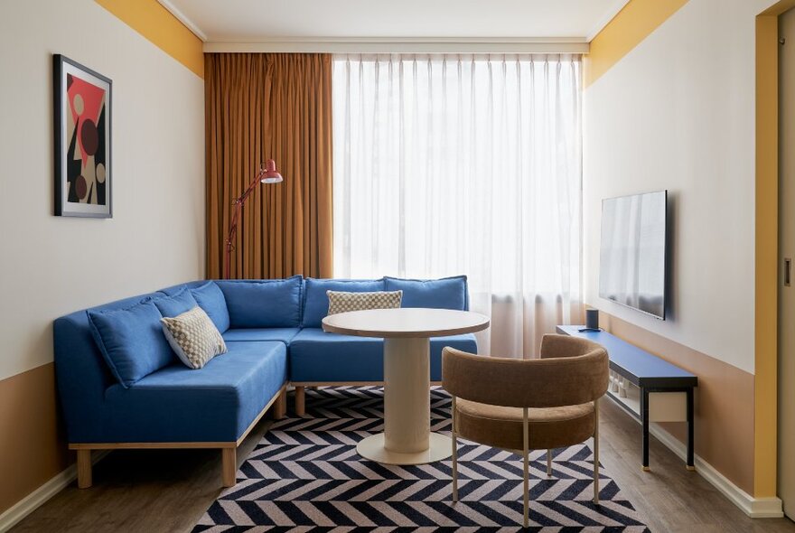 Interior of a hotel room with a blue corner sofa and zig-zag rug. 