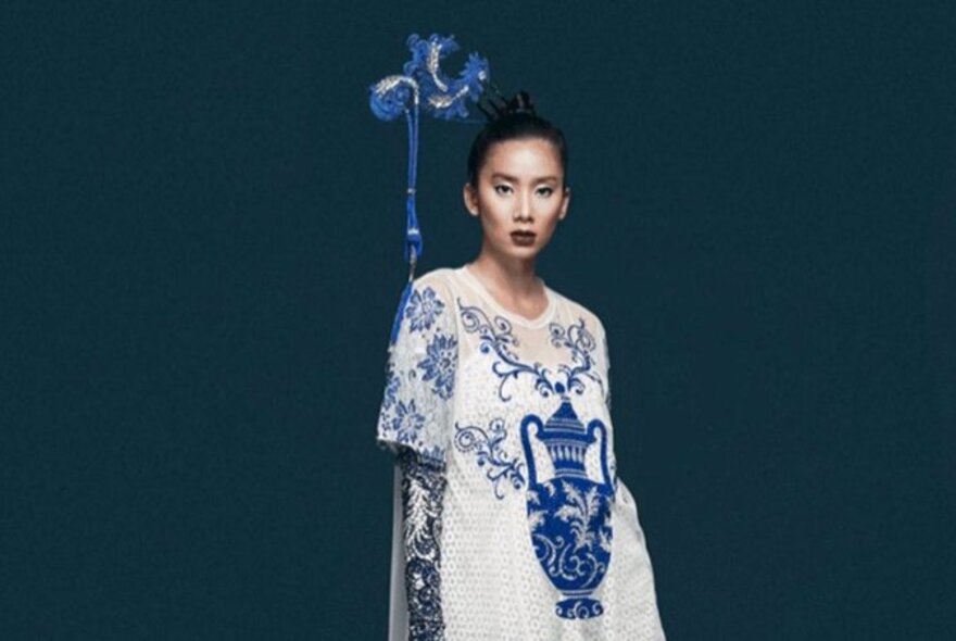 Model wearing a white dress embroidered with blue flowers and vase.